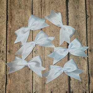 May include: Eight silver satin bows with a striped pattern. The bows are arranged on a wooden surface.