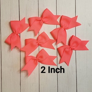 May include: Six 2-inch coral pink hair bows. The bows are made of grosgrain ribbon and have a simple, classic design.