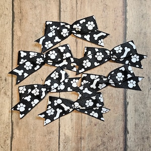 May include: Six black and white bow hair clips with a paw print and bone pattern.
