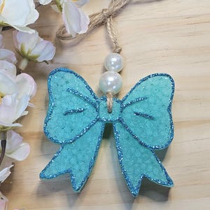 May include: A turquoise glitter bow with a pearl accent hanging from a twine string.