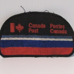May include: A black and red embroidered patch with the text "Canada Post" and "Postes Canada" and a Canadian flag.