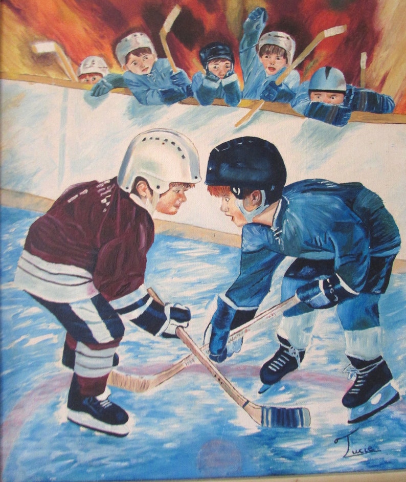 Puede incluir: Dos j&oacute;venes jugadores de hockey con jerseys granate y azul se enfrentan en una pista de hielo azul. Sostienen palos de hockey y llevan cascos. El fondo muestra a un grupo de ni&ntilde;os con uniformes de hockey viendo el partido.