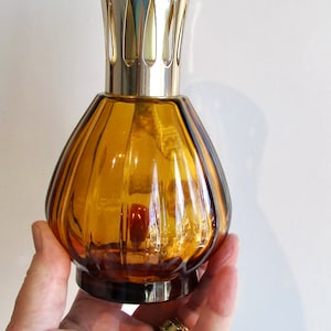 May include: An amber glass oil diffuser bottle with a gold metal lid and a decorative design. The bottle has a ribbed texture.