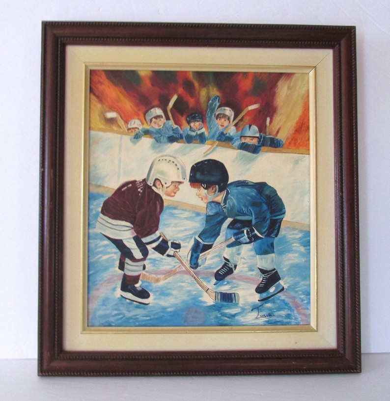 Puede incluir: Una pintura enmarcada de dos j&oacute;venes jugadores de hockey enfrent&aacute;ndose en el hielo. El jugador de la izquierda lleva una camiseta granate y el jugador de la derecha lleva una camiseta azul. Ambos jugadores llevan cascos y sujetan palos de hockey. El fondo muestra a un grupo de otros j&oacute;venes jugadores de hockey viendo el partido.