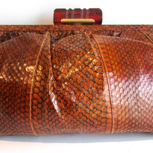 May include: A brown snakeskin clutch bag with a gold clasp and a wooden top handle.