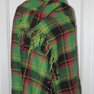 May include: A green, black, red and yellow plaid shawl with fringe. The shawl is draped over a mannequin.
