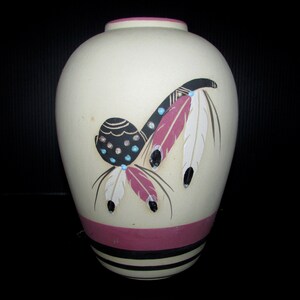 May include: A cream-coloured ceramic vase with a pink rim and a black, white and pink design of feathers and a beaded headdress.