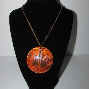 May include: A gold chain necklace with a large, round, orange pendant. The pendant has a textured surface and a black design in the centre.