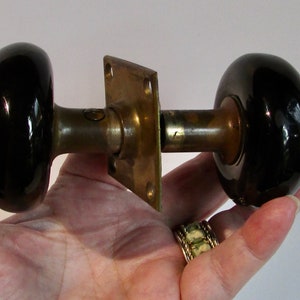 May include: A pair of black ceramic door knobs with a brass backplate and a brass spindle.