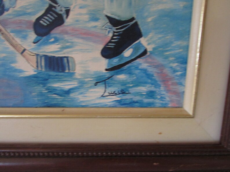 Puede incluir: Una pintura enmarcada de un jugador de hockey patinando sobre hielo. El jugador lleva patines azules y un uniforme blanco. La pintura est&aacute; firmada "Lucie" en la esquina inferior derecha.
