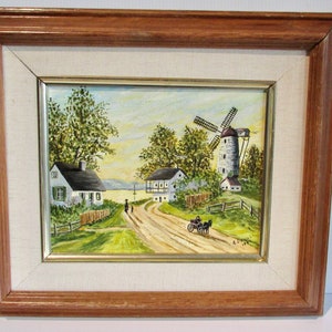 Peut inclure: Une peinture à l'huile encadrée représentant une scène rurale avec un moulin à vent blanc, deux maisons, une calèche tirée par un cheval et deux personnages marchant sur un chemin de terre. La peinture est sur fond de ciel bleu avec des nuages blancs.
