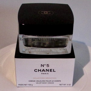 May include: A white box with black trim and the text "N°5 CHANEL PARIS COLLECTION SEDUCTION CREME VELOURS POUR LE CORPS VELVET BODY CREAM POIDS NET 150 g NET WT. 5 OZ." The box contains a clear glass jar with a black lid and the Chanel logo. The jar is filled with a white cream.