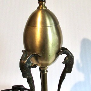 Peut inclure: Une lampe de table dorée avec une base ronde en forme d'œuf et trois pieds décoratifs en forme de griffes. La lampe a un cordon et une prise noirs.