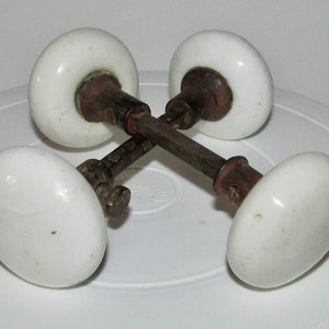 Peut inclure: Quatre boutons de porte en porcelaine blanche avec une tige en métal rouillé. Les boutons sont ronds et ont une finition lisse.