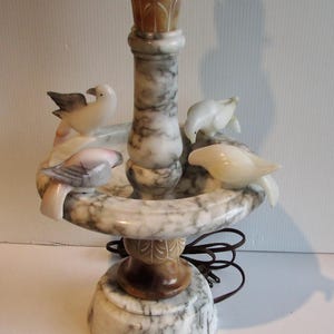 May include: A white alabaster lamp base with a bird bath design. Four small birds are perched on the rim of the bath. The lamp base has a brown and white marbled pattern.