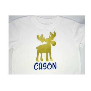 May include: White t-shirt with a gold moose silhouette and the name "CASON" in blue lettering.