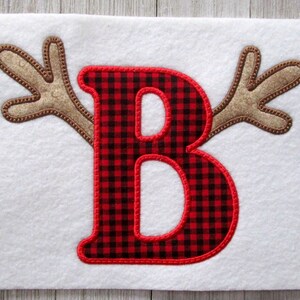 May include: Red and black buffalo check letter B with brown felt antlers on a white background.