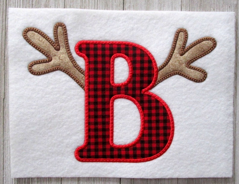 May include: Red and black buffalo check letter B with brown felt antlers on a white background.