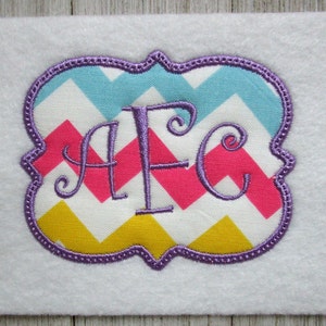 May include: A purple embroidered monogram with the letters "AFC" in a cursive font. The monogram is on a chevron patterned fabric with pink, yellow, blue, and white colors.