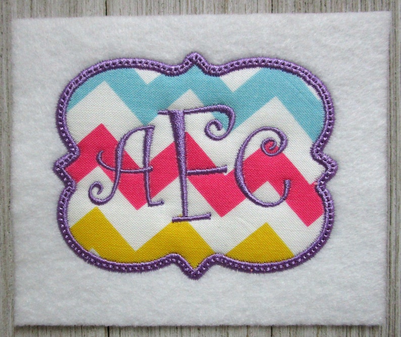 May include: A purple embroidered monogram with the letters "AFC" in a cursive font. The monogram is on a chevron patterned fabric with pink, yellow, blue, and white colors.