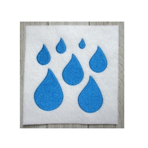 Può includere: Un quadrato di feltro bianco con sette gocce di pioggia ricamate blu di diverse dimensioni.