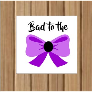 May include: A white square with the text "Bad to the" in black lettering and a purple bow with a black center.