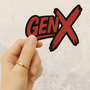 May include: A sticker with the text "GEN X" in red, outlined in black, and a large red "X" symbol. The sticker is held between fingers, with a gold ring on the finger.