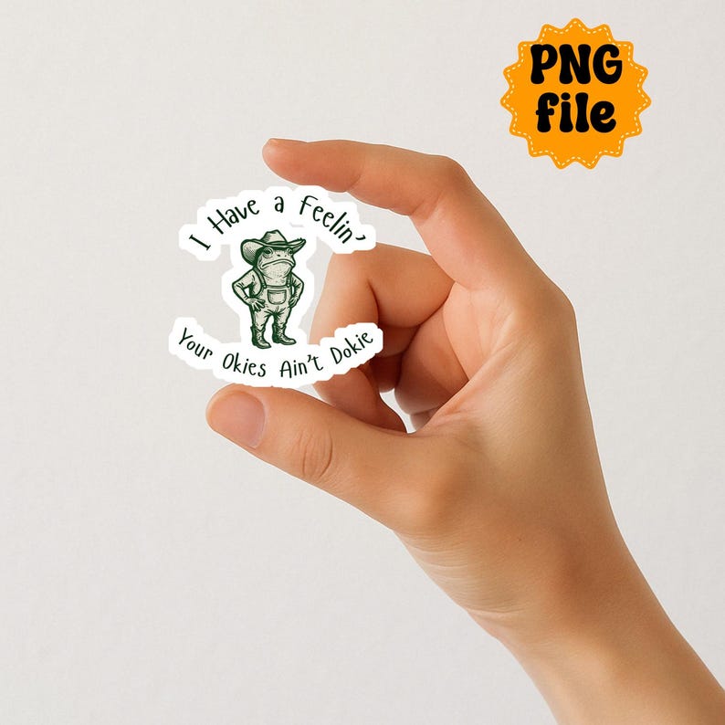 Puede incluir: Una pegatina con una rana de dibujos animados con sombrero de vaquero y peto. La pegatina tiene el texto "I Have a Feelin' Your Okies Ain't Dokie" en un dise&ntilde;o curvo. Un icono de archivo PNG naranja separado est&aacute; en la esquina superior derecha.