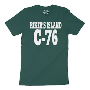 May include: A dark green t-shirt with white text that reads "RIKER'S ISLAND C-76".