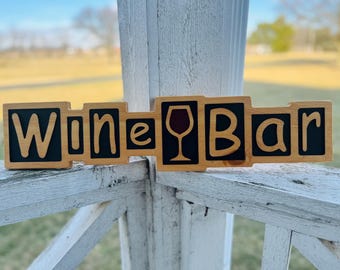 May include: Wooden sign with the words "Wine Bar" in black letters on a light brown background. A red wine glass is depicted between the words.