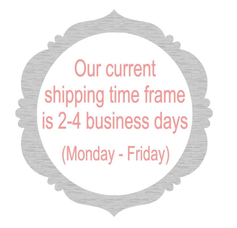 May include: A gray and white decorative sign with a pink text overlay. The text reads "Our current shipping time frame is 2-4 business days (Monday - Friday)"