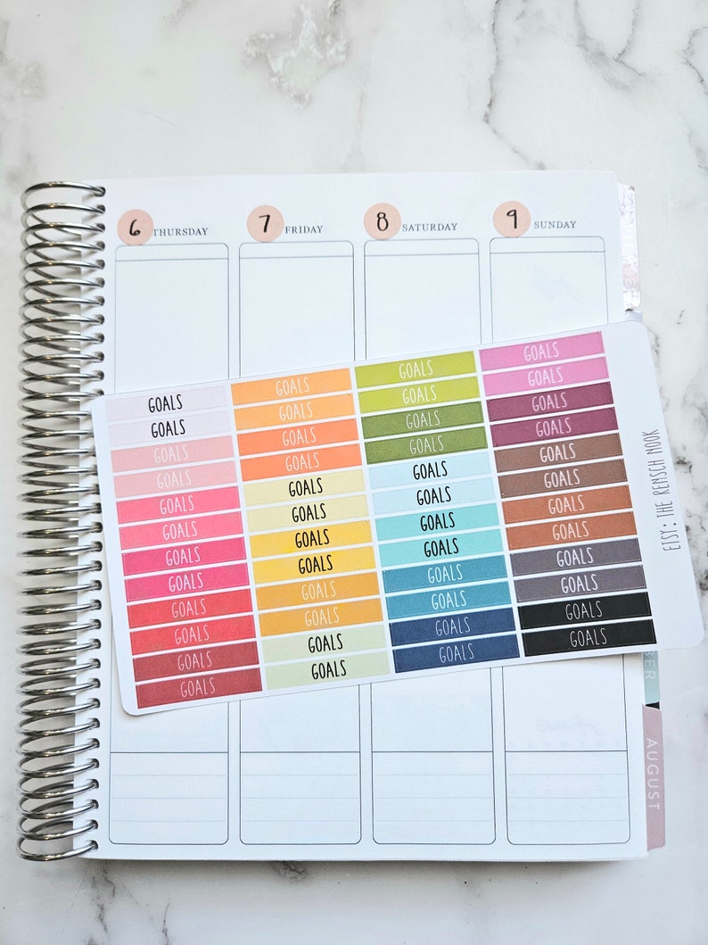 Puede incluir: Una hoja de pegatinas coloridas con la palabra "GOALS" impresa en cada pegatina. Las pegatinas est&aacute;n dispuestas en filas y columnas, con cada fila con un color diferente. Las pegatinas est&aacute;n dise&ntilde;adas para usar en una agenda o diario.