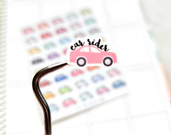May include: A pink car sticker with the text "car rider" in black lettering. The sticker is on a white planner page with a silver tool.