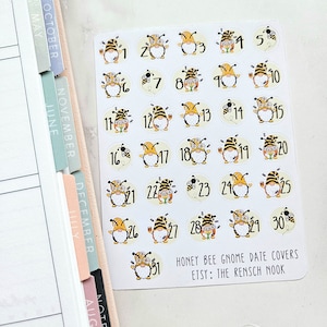 May include: A set of 31 round stickers featuring a bee gnome design. Each sticker has a number from 1 to 31. The stickers are white with a yellow background and feature a gnome wearing a red hat and holding a honey pot. The text "Honey Bee Gnome Date Covers" and "Etsy: The Rensch Nook" is printed at the bottom of the sheet.