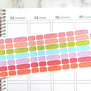 May include: A rectangular sheet of small, colorful adhesive planner stickers featuring the words QUIZ, TEST, and HOMEWORK in a handwritten font. The stickers are arranged in rows with various colors including pink, orange, green, blue, purple, and red.