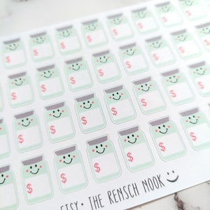 May include: Sheet of stickers featuring smiling jar illustrations with dollar signs. The jars are light green with gray lids and pink accents. The text "ETSY: THE RENSCH NOOK" is printed at the bottom.