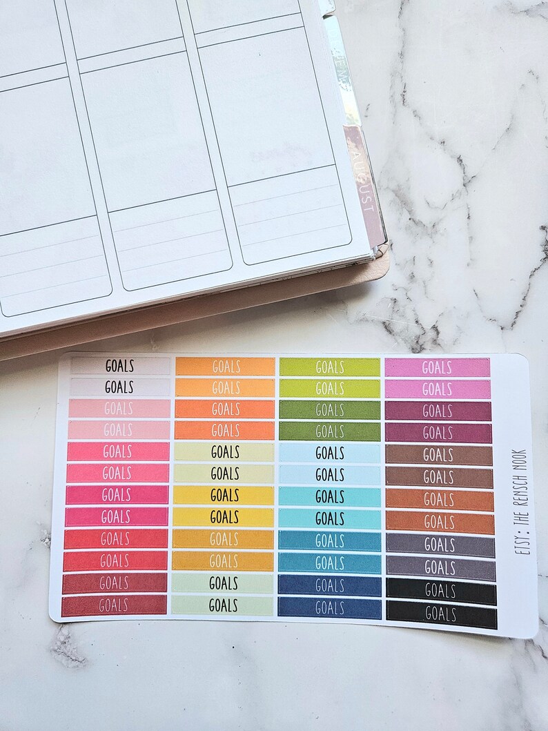 Puede incluir: Una hoja de pegatinas de colores con la palabra "GOALS" impresa en cada pegatina. Las pegatinas est&aacute;n dispuestas en filas de cuatro, con cada fila presentando un color diferente. Los colores incluyen rosa, naranja, amarillo, verde, marr&oacute;n, rojo, azul y gris. Las pegatinas est&aacute;n dise&ntilde;adas para su uso en una agenda o diario.