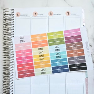Puede incluir: Una hoja de pegatinas coloridas con la palabra "GOALS" impresa en cada pegatina. Las pegatinas est&aacute;n dispuestas en filas y columnas, con cada fila presentando un color diferente. Las pegatinas est&aacute;n dise&ntilde;adas para ser usadas en una agenda o diario.