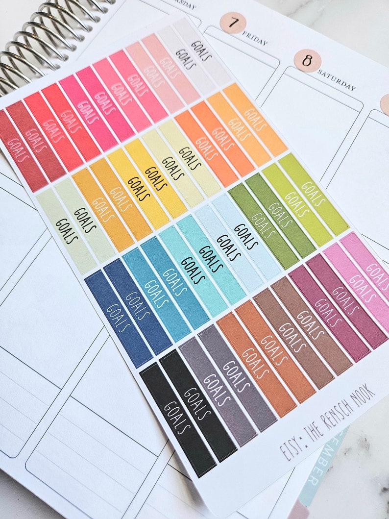 Puede incluir: Una hoja de pegatinas coloridas con la palabra "GOALS" impresa en cada pegatina. Las pegatinas est&aacute;n dispuestas en filas y columnas, con cada fila presentando un color diferente. Las pegatinas est&aacute;n dise&ntilde;adas para su uso en una agenda o diario.