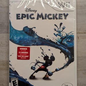 May include: A sealed Disney Epic Mickey video game case for the Wii console. The cover features Mickey Mouse holding a paintbrush with blue paint splashes, Oswald the Lucky Rabbit, and a red sticker stating Winner of over 15 awards including Best Wii Game.