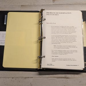 May include: A black three-ring binder containing technical documentation titled Problem Determination Procedures. The open manual features white pages with black text, a yellow divider, and a small white card with printed text.