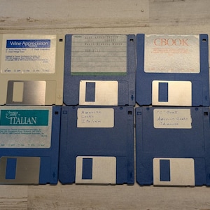 May include: Six 3.5-inch floppy disks arranged in two rows. One is beige, five are blue. Labels include Wine Appreciation Series, CBOOK, and Italian. Handwritten text on three labels reads Wine Appreciation Series, American Cooks Italian, and CBook American Cooks Chinese.