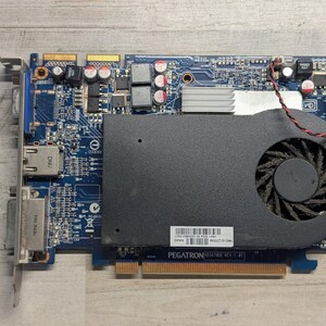 May include: A blue printed circuit board graphics card featuring a black cooling shroud with an integrated fan, a silver heatsink, and a metal mounting bracket with output ports. A white sticker with a barcode and the text PEGATRON is visible.