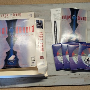 May include: A PC game box set for Angel Devoid: Face of the Enemy, including the cardboard box, a manual, and four CD-ROM discs in individual paper sleeves. The box features two large faces in profile, the game title in red text, and a small hospital bed.