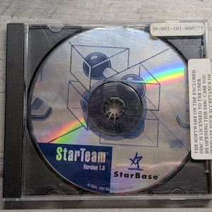 May include: A StarTeam Version 1.0 software CD in a clear plastic jewel case. The disc features a blue and white graphic of geometric shapes and spheres. A white sticker on the right side contains text regarding software licensing and acceptance.