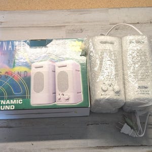 May include: A pair of white computer speakers with attached white power and audio cables, partially wrapped in clear plastic, next to their original cardboard box labeled DYNAMIC SOUND with a graphic of the speakers on the front panel.