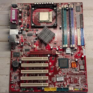 May include: A red MSI 865PE Neo2-P motherboard featuring a central processor socket, a silver heatsink, four memory slots in blue and teal, multiple white PCI expansion slots, and various integrated ports including a purple parallel port.