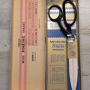 May include: Vintage Wiss Pinking Shears Model C with black handles, presented in an original cardboard box. The packaging features blue and tan graphics with text including Wiss Pinking Shears, CB-9, and details about the hot-forged steel construction.