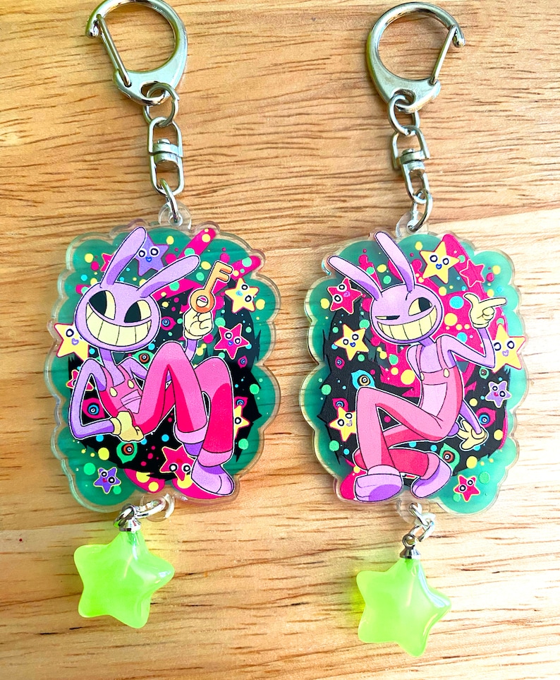 May include: Two keychains featuring a cartoon character with a purple head and pink body, holding a key or pointing. The keychains have a green border with stars and a neon green star charm. The keychains are attached to a silver clasp.