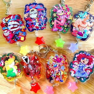 May include: A collection of colorful acrylic keychains featuring cartoon characters. Each keychain has a unique design with vibrant colors and is adorned with a star-shaped charm. The keychains are attached to silver-colored metal rings.